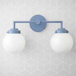 May include: A blue wall sconce with two white glass globe shades. The sconce has a simple, modern design and is perfect for adding a touch of style to any room.