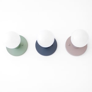 May include: Three wall sconces with white globe light bulbs. The sconces have different colored bases: green, blue, and brown.