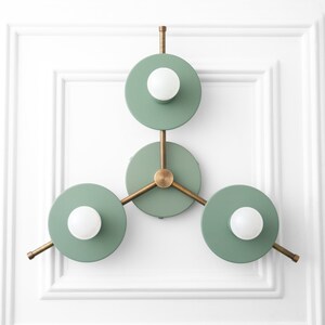 May include: A modern wall sconce with three circular light fixtures. The fixtures are painted a light green color and have a brass finish. Each fixture has a single light bulb.