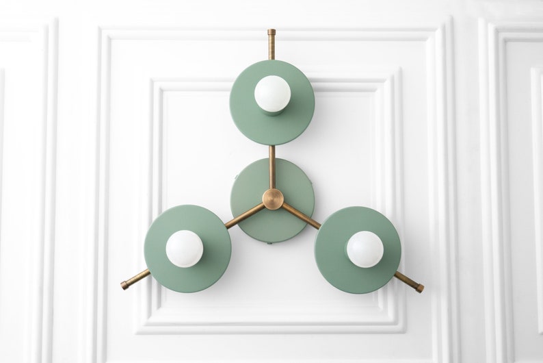 May include: A modern wall sconce with three circular light fixtures. The fixtures are painted a light green color and have a brass finish. Each fixture has a single light bulb.
