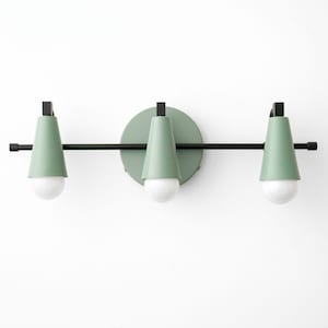 May include: A modern, three-light vanity fixture. The fixture features three light green, cone-shaped shades with white bulbs, mounted on a black bar. A circular light green base is centered on the bar. The fixture is mounted on a white wall.