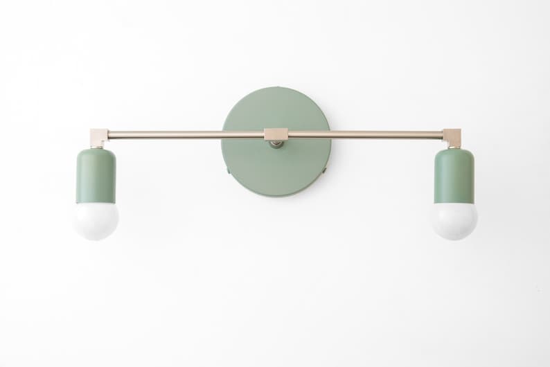 Puede incluir: Una l&aacute;mpara de pared con dos bombillas. La l&aacute;mpara tiene un acabado en n&iacute;quel cepillado y una pantalla de color verde salvia. Las bombillas son blancas.