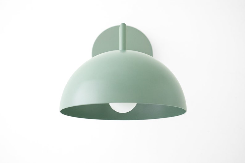 Puede incluir: Una l&aacute;mpara de pared de color verde claro en forma de c&uacute;pula con una bombilla blanca. La l&aacute;mpara tiene un dise&ntilde;o simple y moderno.