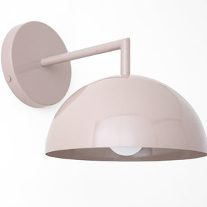 Puede incluir: Una l&aacute;mpara de pared de color rosa claro con una pantalla en forma de c&uacute;pula y un brazo curvo.