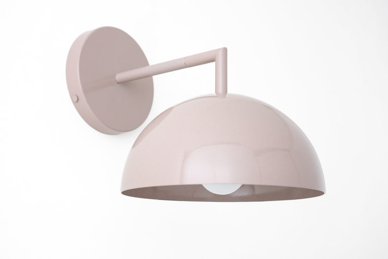 Puede incluir: Una l&aacute;mpara de pared de color rosa claro con una pantalla en forma de c&uacute;pula y un brazo curvo.