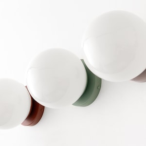 Peut inclure: Trois luminaires &agrave; globe blanc avec des bases de couleurs diff&eacute;rentes. Les bases sont marron, verte et marron.
