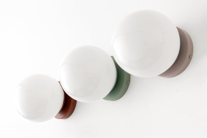 Peut inclure: Trois luminaires &agrave; globe blanc avec des bases de couleurs diff&eacute;rentes. Les bases sont marron, verte et marron.