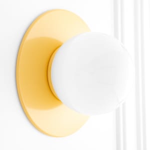 May include: A yellow round wall sconce with a white globe light fixture.