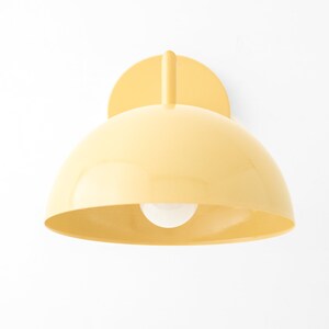 Puede incluir: Una l&aacute;mpara de pared de forma de c&uacute;pula amarilla con una sola bombilla.