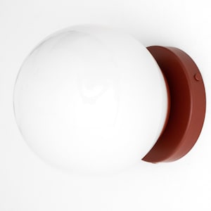 Peut inclure: Un luminaire globe blanc avec une base en terre cuite. Le luminaire est mont&eacute; sur un mur blanc.