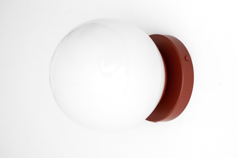 Peut inclure: Un luminaire globe blanc avec une base en terre cuite. Le luminaire est mont&eacute; sur un mur blanc.