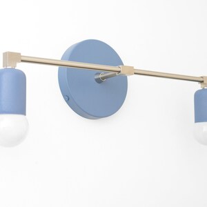 Puede incluir: Una l&aacute;mpara de pared con dos bombillas pintadas de azul y un brazo de metal plateado. La l&aacute;mpara tiene una placa trasera redonda pintada de azul.