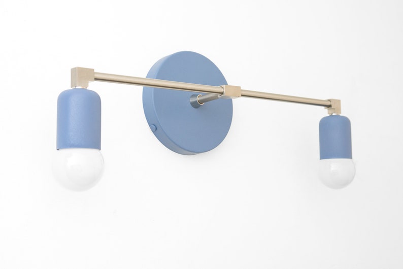 Puede incluir: Una l&aacute;mpara de pared con dos bombillas pintadas de azul y un brazo de metal plateado. La l&aacute;mpara tiene una placa trasera redonda pintada de azul.