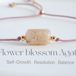 Puede incluir: Una pulsera de ágata flor con un cordón rosa y cuentas doradas. La piedra central es de color melocotón claro y de forma cilíndrica. El texto en la imagen dice "Flower blossom Agate" y "Self-Growth Resolution Balance."
