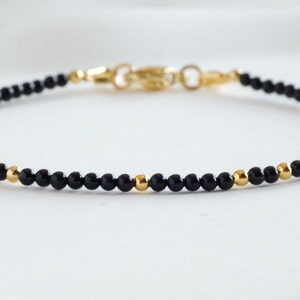 Puede incluir: Delicada pulsera de cuentas negras con detalles dorados y un cierre dorado. La pulsera presenta pequeñas cuentas negras redondas intercaladas con cuentas doradas.