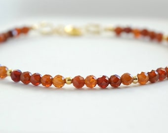 May include: A delicate bracelet featuring small, faceted, reddish-brown gemstone beads interspersed with gold-colored beads. The bracelet is strung on a fine chain and has a gold clasp. The gemstones have a warm, earthy tone.