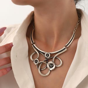 May include: A silver statement necklace with a geometric design featuring multiple circles and a central flower-shaped pendant.