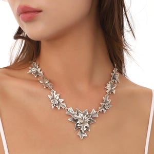 May include: A silver necklace with a pendant made of multiple leaf shapes. The leaves are arranged in a cascading pattern, with the largest leaf at the bottom.