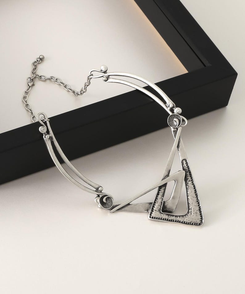 May include: A silver-toned necklace with a geometric triangle pendant. The pendant is made of two overlapping triangles with a textured surface.