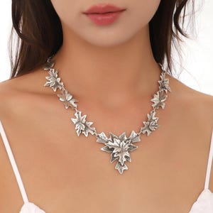 May include: A silver necklace with a large, detailed leaf pendant and smaller leaf accents along the chain.