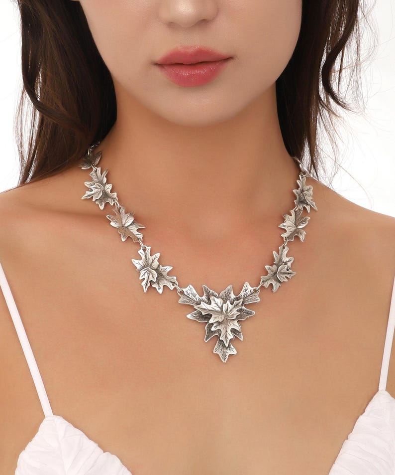 May include: A silver necklace with a large, detailed leaf pendant and smaller leaf accents along the chain.