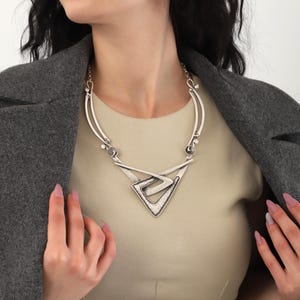 May include: A silver statement necklace with a geometric design. The necklace features a large triangular pendant with a textured surface.