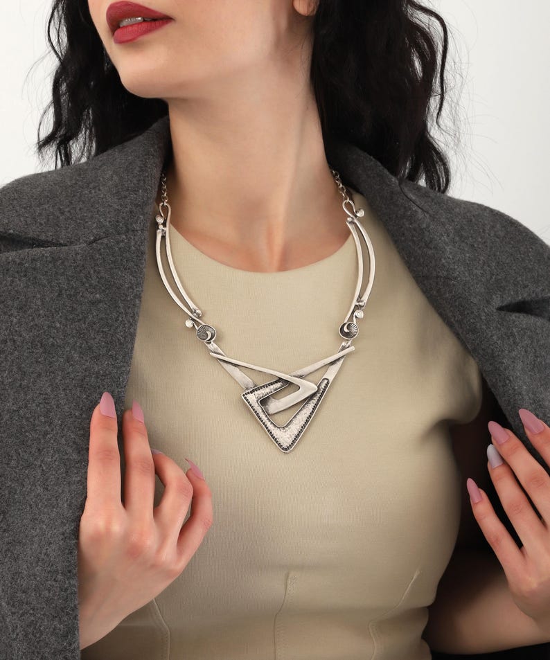 May include: A silver statement necklace with a geometric design. The necklace features a large triangular pendant with a textured surface.