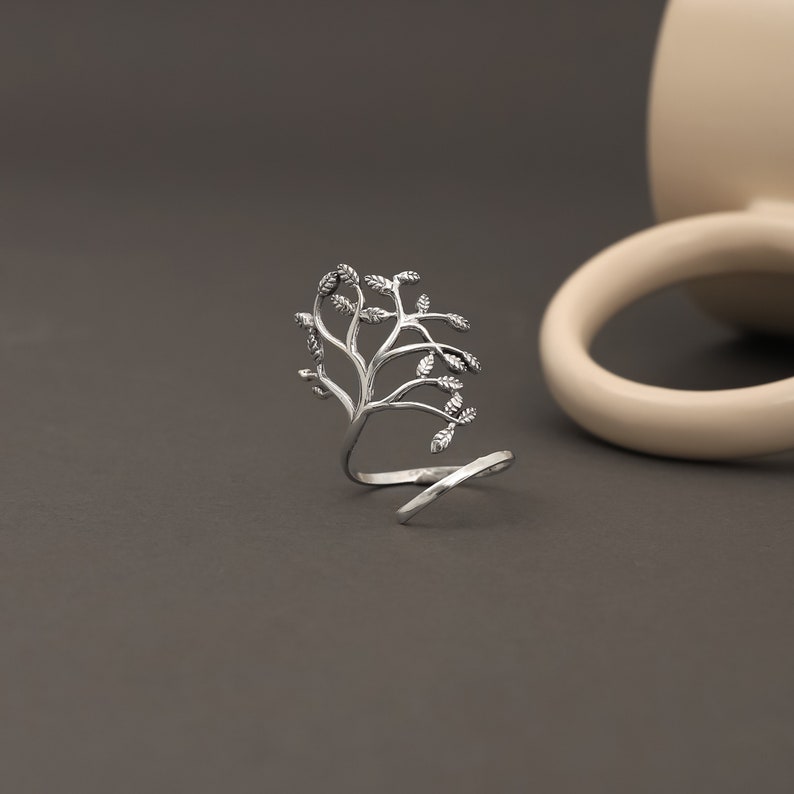 May include: Silver ring with a tree branch design. The ring is open and wraps around the finger.