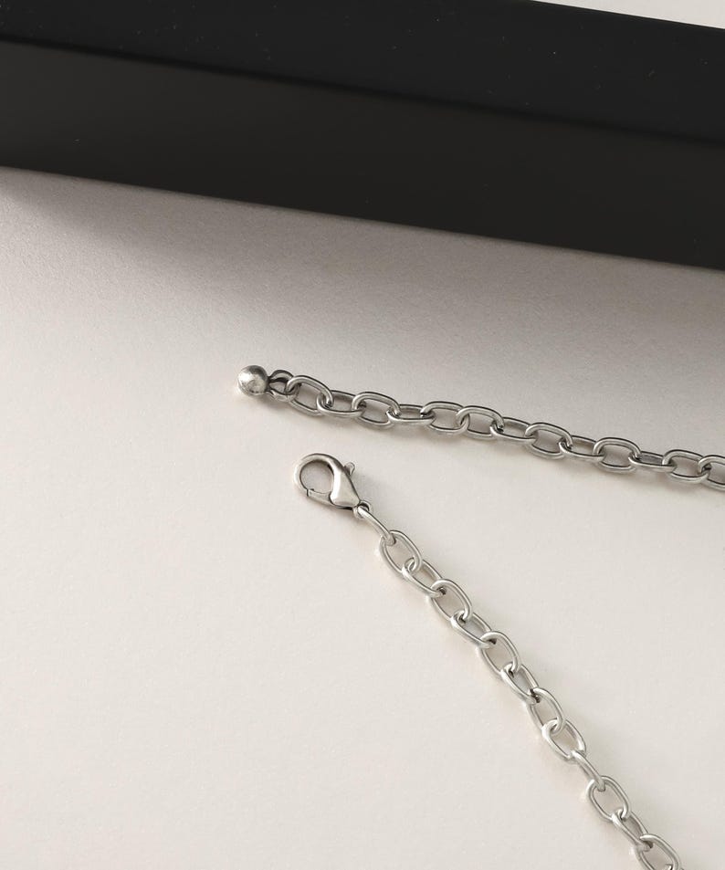 May include: A silver chain necklace with a lobster clasp and a small ball at the end. The chain is made of small, linked circles.