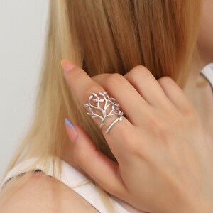 May include: A silver ring with a tree branch design. The ring is open and adjustable to fit different finger sizes.