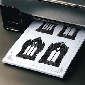 Pu&ograve; includere: Una stampante nera stampa una pila di carta bianca con disegni di cornici di finestre gotiche. I disegni variano nello stile, con dettagli ornati e pi&ugrave; semplici. La carta ha bordi decorativi.