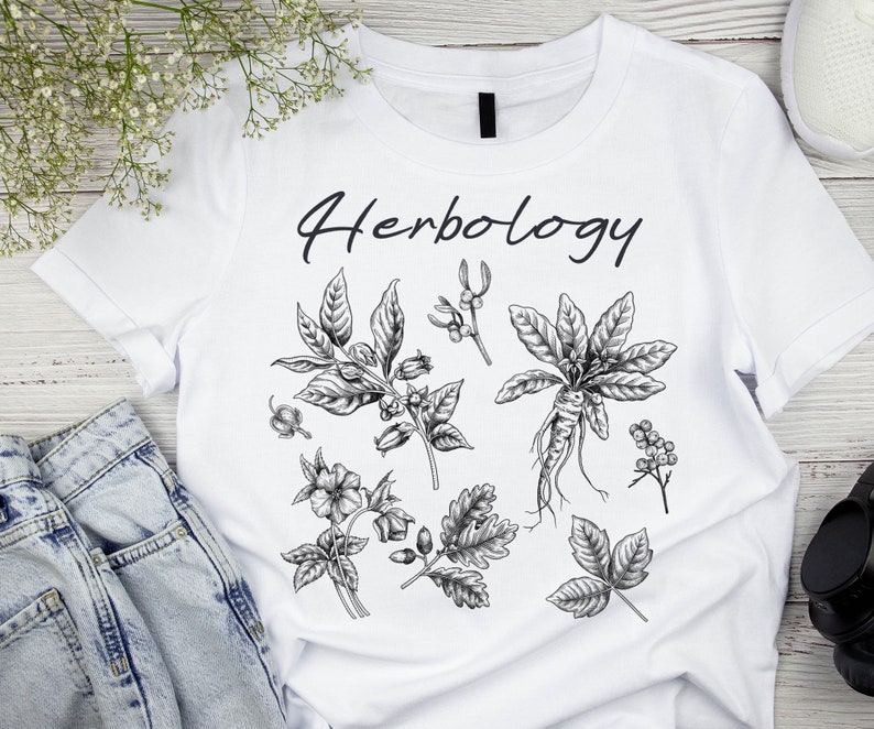 May include: White t-shirt with the word "Herbology" printed in black. The shirt features a black and white illustration of various herbs and plants.