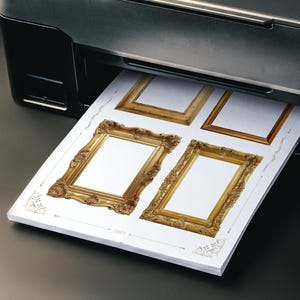 May include: A black printer producing a sheet of paper featuring four decorative gold picture frame designs. The frames, with detailed ornamentation, are set against a white backdrop. The paper is emerging from the printer.