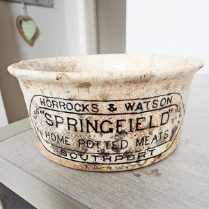 Peut inclure: Bol en céramique crème antique avec une finition craquelée et vieillie. Le bol porte une étiquette noire et blanche avec le texte "HORROCKS & WATSON SPRINGFIELD HOME POTTED MEATS SOUTHPORT".