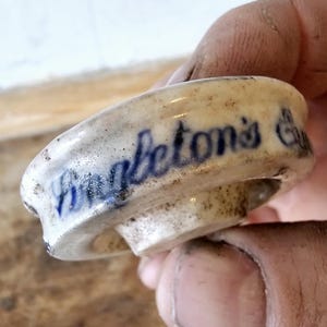 Puede incluir: Un tapón de botella de cerámica blanca con letras azules que dice "Robertson's Extract".