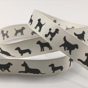May include: Cream-coloured ribbon featuring a repeating pattern of black dog silhouettes. The ribbon is curled, displaying various dog breeds in profile, including dachshunds and poodles. The ribbon is approximately 2.5 cm wide.