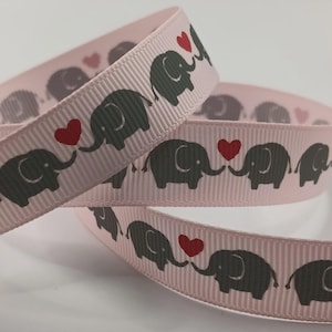 May include: Pale pink ribbon with a repeating pattern of grey elephants and red hearts. The elephants' trunks touch the hearts. The ribbon has a ribbed texture, suitable for crafts or gift wrapping.