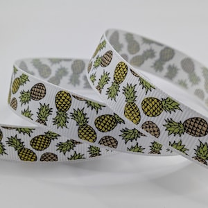 May include: White ribbon featuring a repeating pattern of yellow and brown pineapples with green leaves. The ribbon is curled, displaying the design on both sides. Suitable for crafts or gift wrapping.
