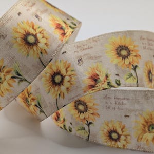 Op de afbeelding: Rol decoratief lint met een herhalend patroon van gele zonnebloemen op een beige achtergrond. Het lint heeft ook kleine tekst en vlinder illustraties. Geschikt voor knutselen.
