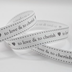 May include: White ribbon featuring the text "to love & to cherish" in grey, accompanied by heart symbols. The ribbon is curled and has a dotted border.