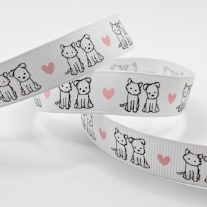 May include: White ribbon featuring a repeating pattern of black line-drawn puppies and pink hearts. The ribbon is curled and layered, displaying the design. The puppies are shown in pairs, creating a playful and charming aesthetic.