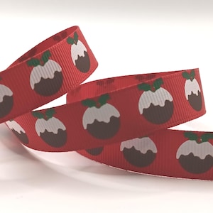 May include: A red grosgrain ribbon featuring a repeating pattern of brown Christmas puddings topped with white icing and green holly leaves. The textured fabric ribbon is coiled, displaying the festive holiday print across its surface.