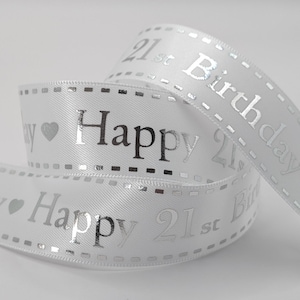 May include: White satin ribbon with silver text reading "Happy 21st Birthday". The ribbon is curled, featuring a dotted border and a heart symbol. Ideal for wrapping gifts or decorations.
