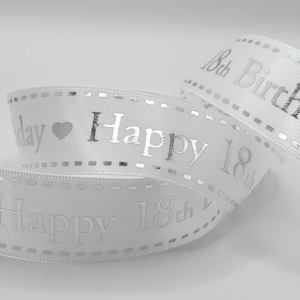 May include: White satin ribbon with silver text reading "Happy 18th Birthday". The ribbon is curled and has a dotted border. A heart symbol is next to the word "day".