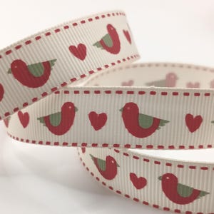 May include: Cream-coloured ribbon featuring a pattern of red birds and hearts. The ribbon has a ribbed texture and is edged with a dotted red line. Suitable for crafts and gift wrapping.