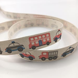 May include: Beige ribbon with a repeating pattern of cartoon vehicles, including a red double-decker bus, police cars, and trucks. This ribbon is suitable for crafting and adding a playful touch to various projects. The ribbon is measured in centimeters.