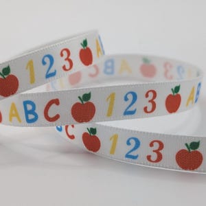 May include: White ribbon featuring the letters ABC, numbers, and red apple illustrations. The ribbon is curled, suggesting it's made of a smooth, woven material. Ideal for school or craft projects.
