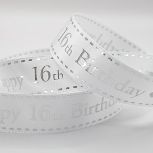 May include: White satin ribbon with silver text reading "Happy 16th Birthday." The ribbon is curled and layered, with a dotted border. The text is in a classic serif font, suitable for a celebration.