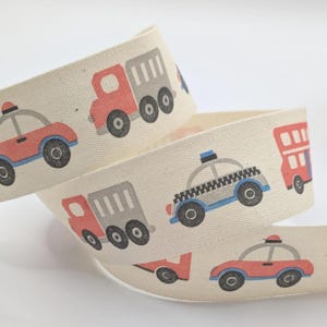 May include: Cream-coloured ribbon with a repeating pattern of vehicles in red, grey, and blue. The design includes cars, trucks, police cars, and buses. Suitable for crafts, this ribbon adds a playful touch to projects.