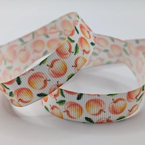 May include: A white grosgrain ribbon featuring a repeating pattern of watercolor-style peaches in shades of orange, yellow, and pink, accented with small green leaves. The ribbon has a textured, ribbed surface and is coiled in a loop.